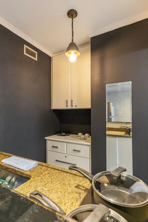 A modern kitchen with a granite countertop, a sink, a stove, and a hanging light fixture. - Matiz Manhattan Hotel - Gym Pool & Sauna (São Paulo)