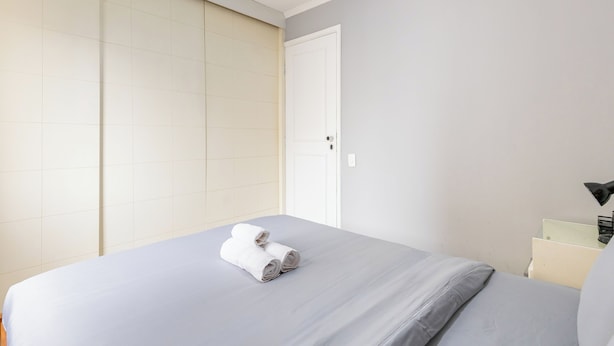 Una habitación de hotel con una cama, una mesita de noche, una lámpara y una puerta.