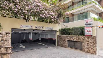 Entrada de um estacionamento com placas de sinalização, um muro de pedra e um edifício com varandas.