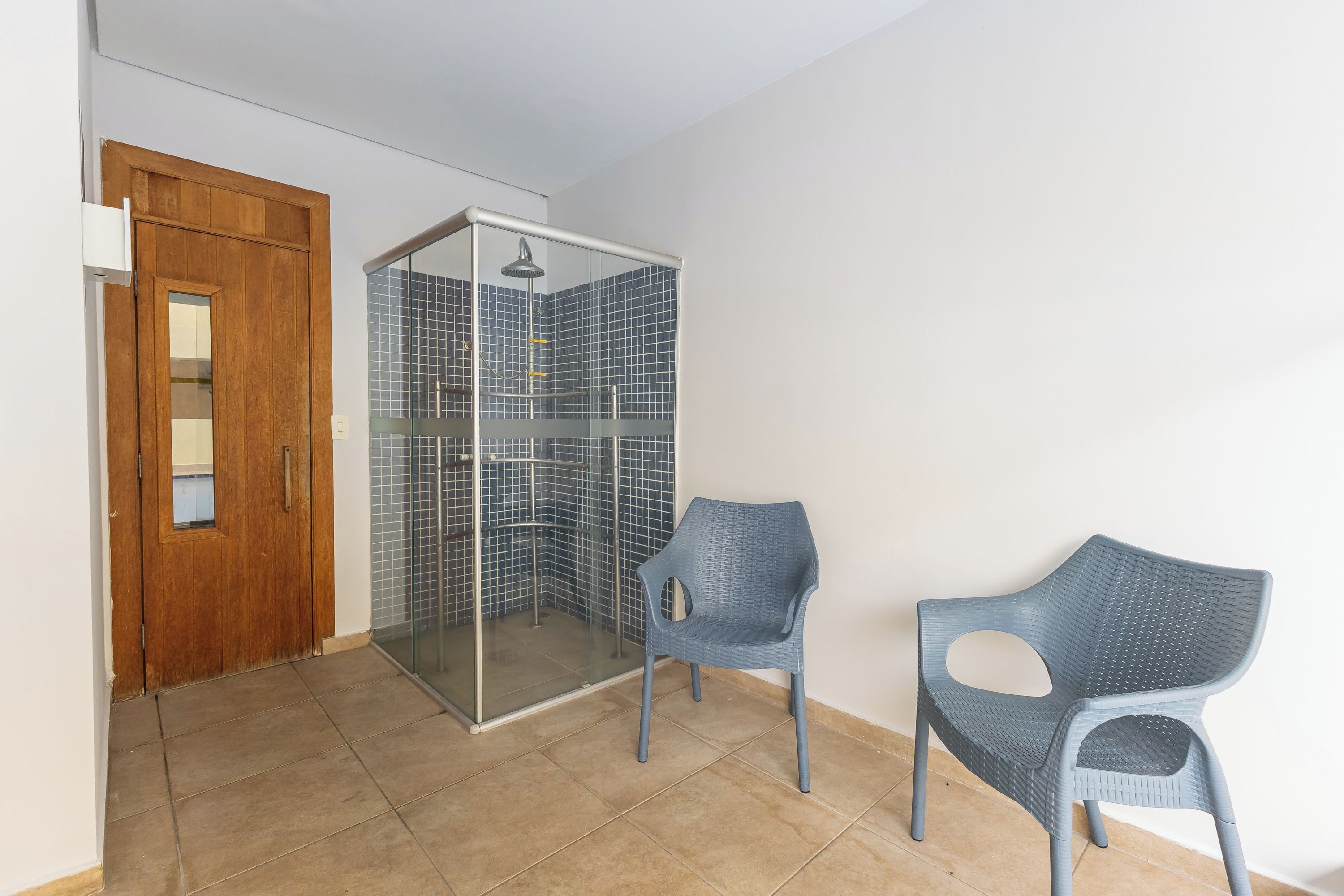 Quarto com porta de madeira, box de chuveiro com azulejos azuis e duas cadeiras azuis.