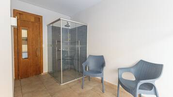 Quarto com porta de madeira, box de chuveiro com azulejos azuis e duas cadeiras azuis.