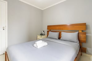 Habitación individual con una cama de una sola plaza, cabecera de madera, mesita de noche con lámpara y una cama bien hecha con toallas blancas enrolladas.