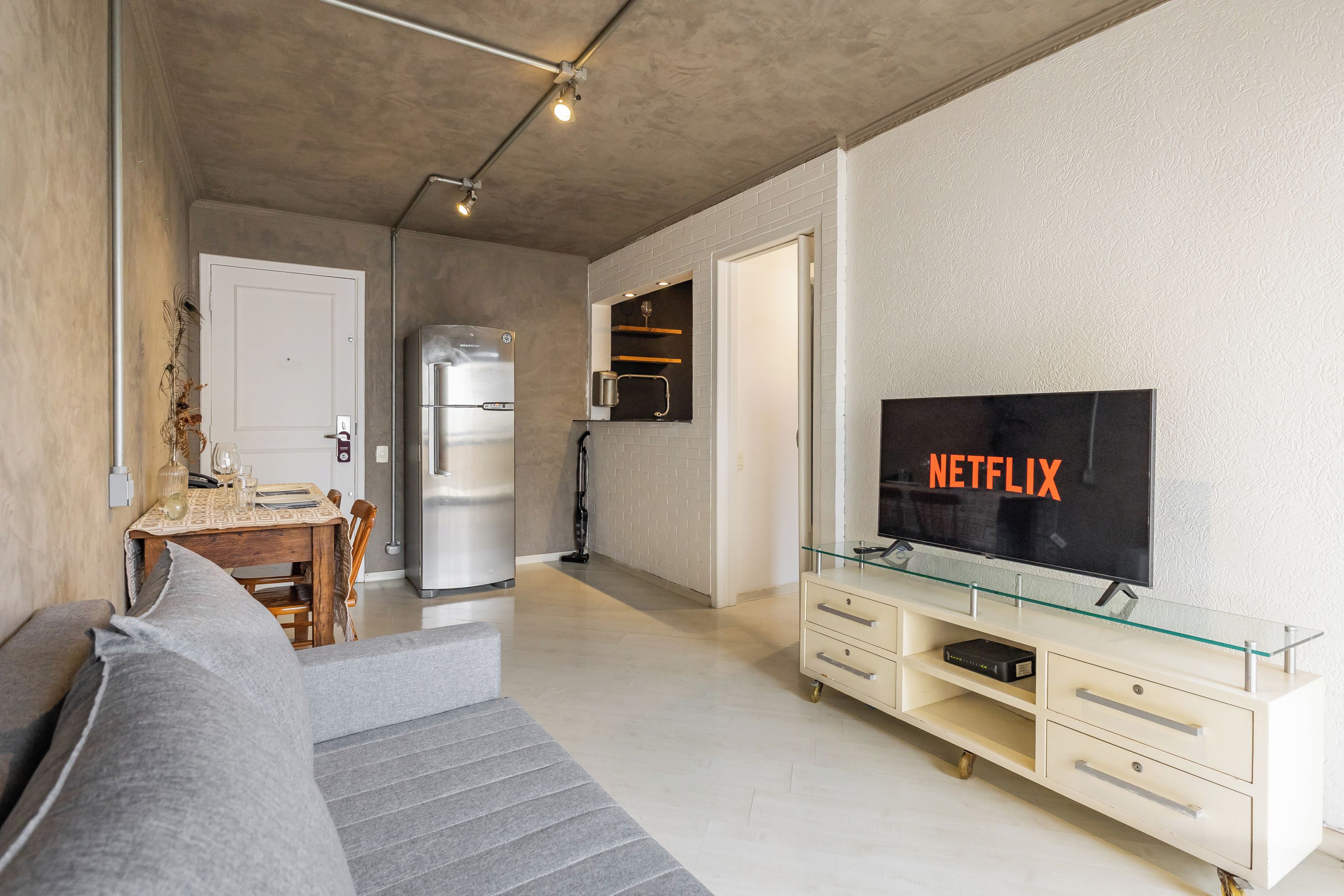 A modern living room with a sofa, a glass TV stand, and a flat-screen TV displaying 'NETFLIX'.