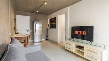 A modern living room with a sofa, a glass TV stand, and a flat-screen TV displaying 'NETFLIX'.
