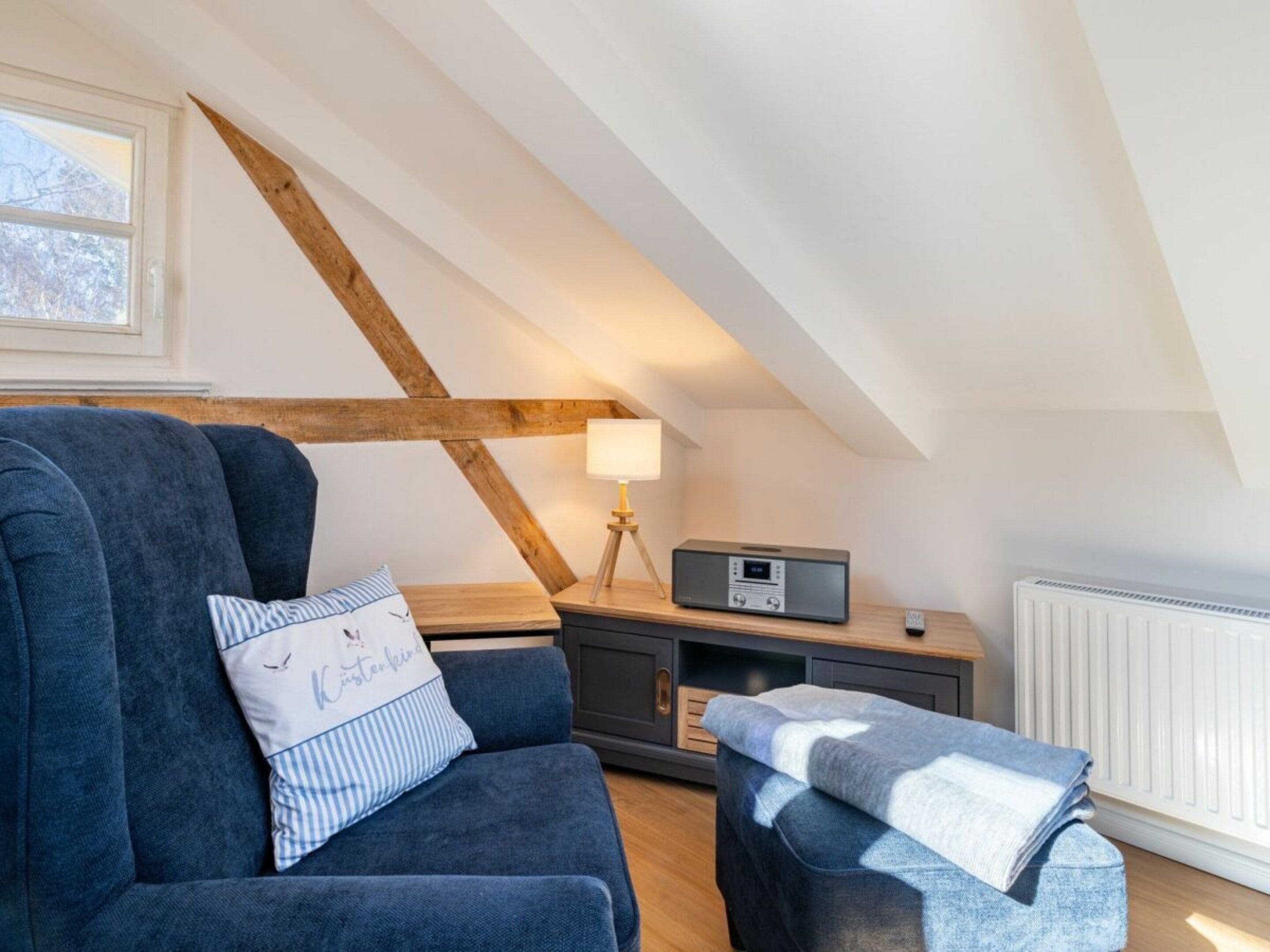 Une chambre à coucher confortable, aménagée en mezzanine, avec un plafond en pente, un canapé bleu foncé, une petite table avec une lampe et une radio.