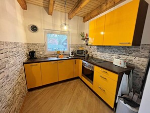 A kitchen with yellow cabinets, a stone wall, a window, and a clock. - Holiday Apartment With 1 Bedroom (Zirchow)
