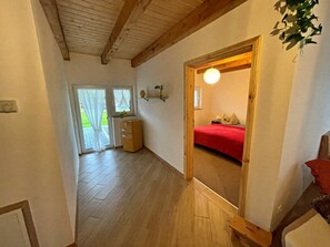 A hallway with wooden flooring leading to a bedroom with a red bedspread and a small bedside table. - Holiday Apartment With 1 Bedroom (Zirchow)