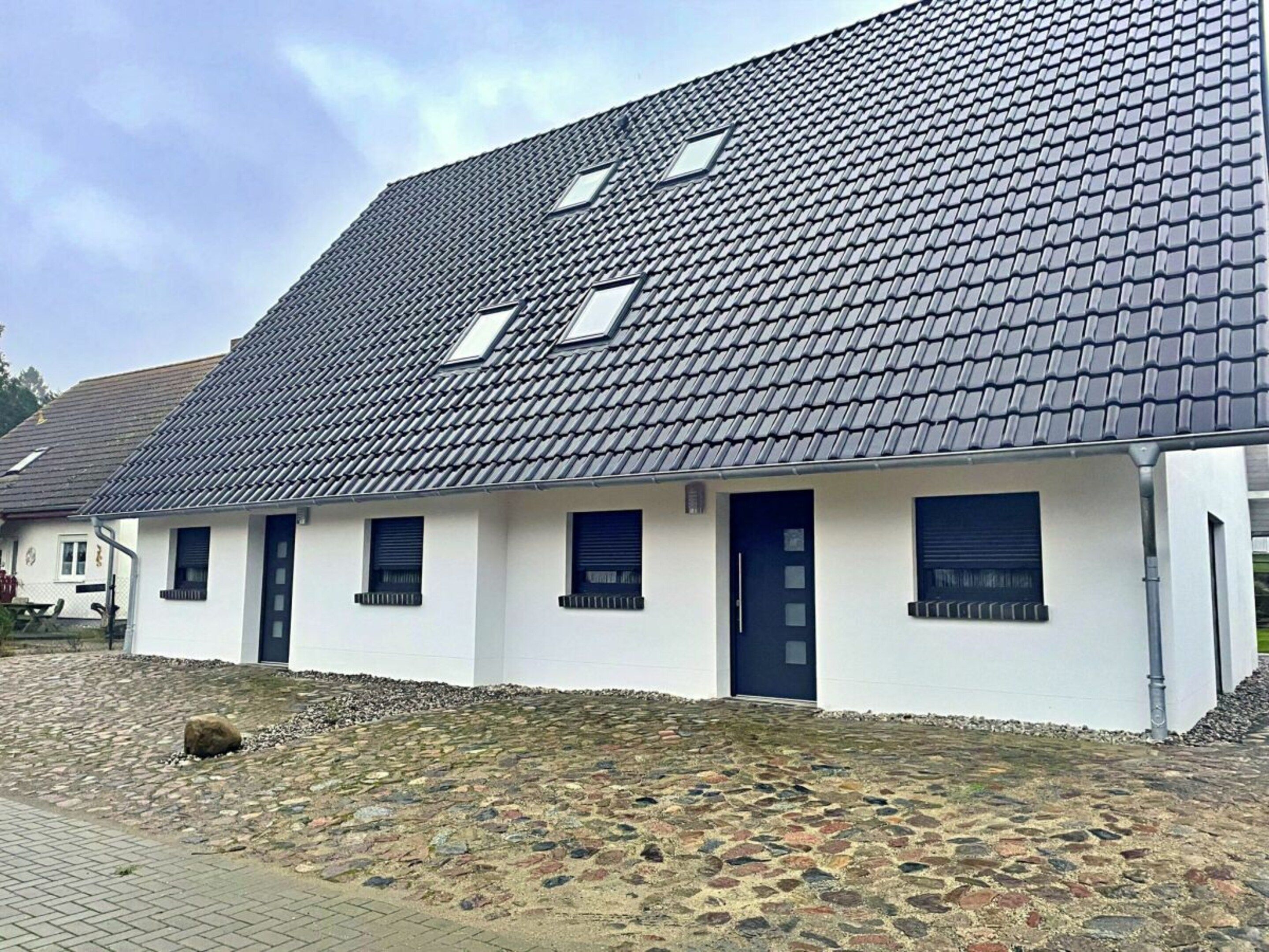 A modern building with a sloped roof, multiple windows, and a paved entrance area.