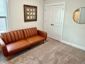 A brown leather sofa against a wall with a framed picture, a white door, and a round mirror. - Fully Furnished Retreat In The Heart Of Charlotte (Charlotte)