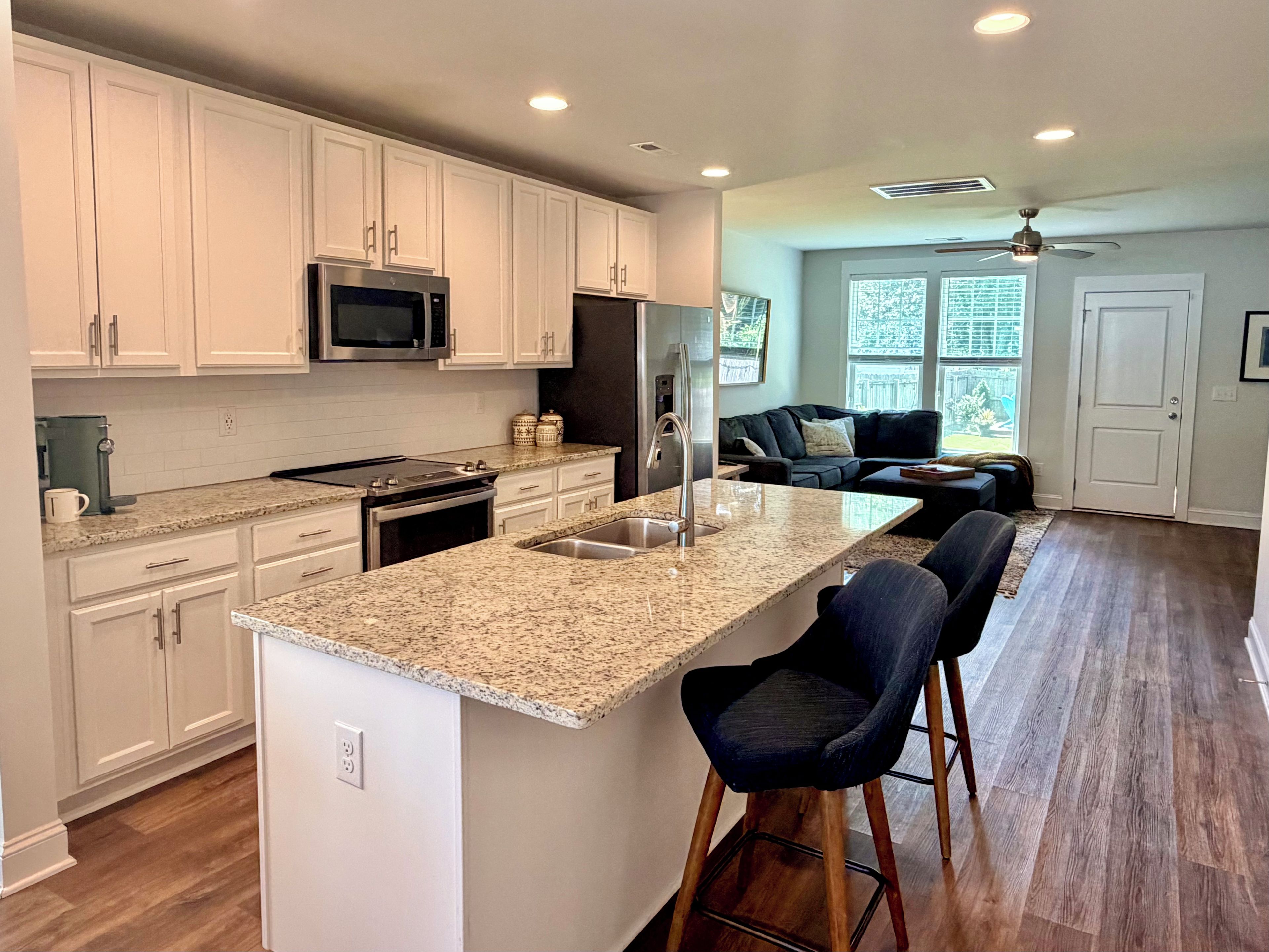 A modern kitchen with white cabinetry, a granite countertop, a built-in microwave, and a stainless steel sink.