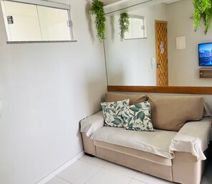 A beige sofa with a leaf-patterned pillow, a wooden headboard, a television, and a mirror reflecting a door and a window. - 402 Functional and Welcoming. (Belém)