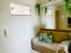 Une pièce comprenant un canapé, un miroir, un téléphone fixé au mur et des plantes suspendues.