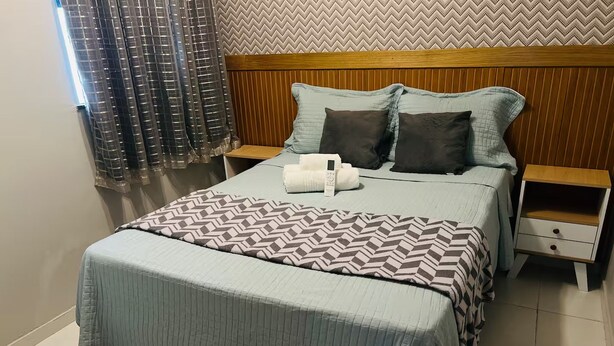 A neatly made bed with a patterned bedspread, two pillows, and a remote control on the side. - 402 Functional and Welcoming. (Belém)