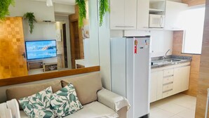 A living room with a sofa, a television, and a kitchen area with a refrigerator and microwave. - 402 Functional and Welcoming. (Belém)