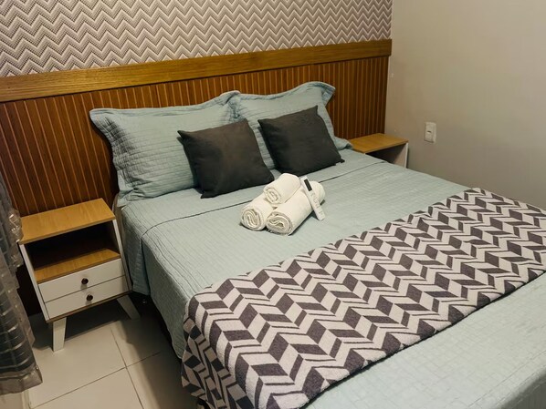 Un lit bien fait, avec une couvre-lit à motifs, deux oreillers et une serviette enroulée posée sur une tête de lit en bois.