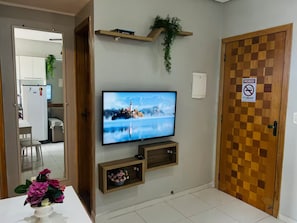 A living room with a television mounted on the wall, a wooden door with a prohibition sign, and a small shelf with a plant. - 402 Functional and Welcoming. (Belém)