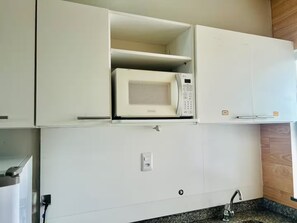 Une cuisine avec un four à micro-ondes posé sur un meuble blanc, un four encastré en dessous, et un plan de travail en granit avec un évier.