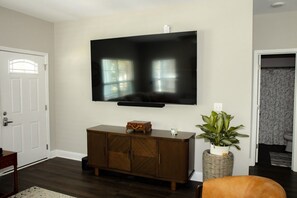 A living room with a flat-screen TV mounted on the wall, a wooden cabinet with a plant, and a door leading to another room. - Brand-New Family-Friendly Home 5 Minutes to USC & Downtown (Cayce)