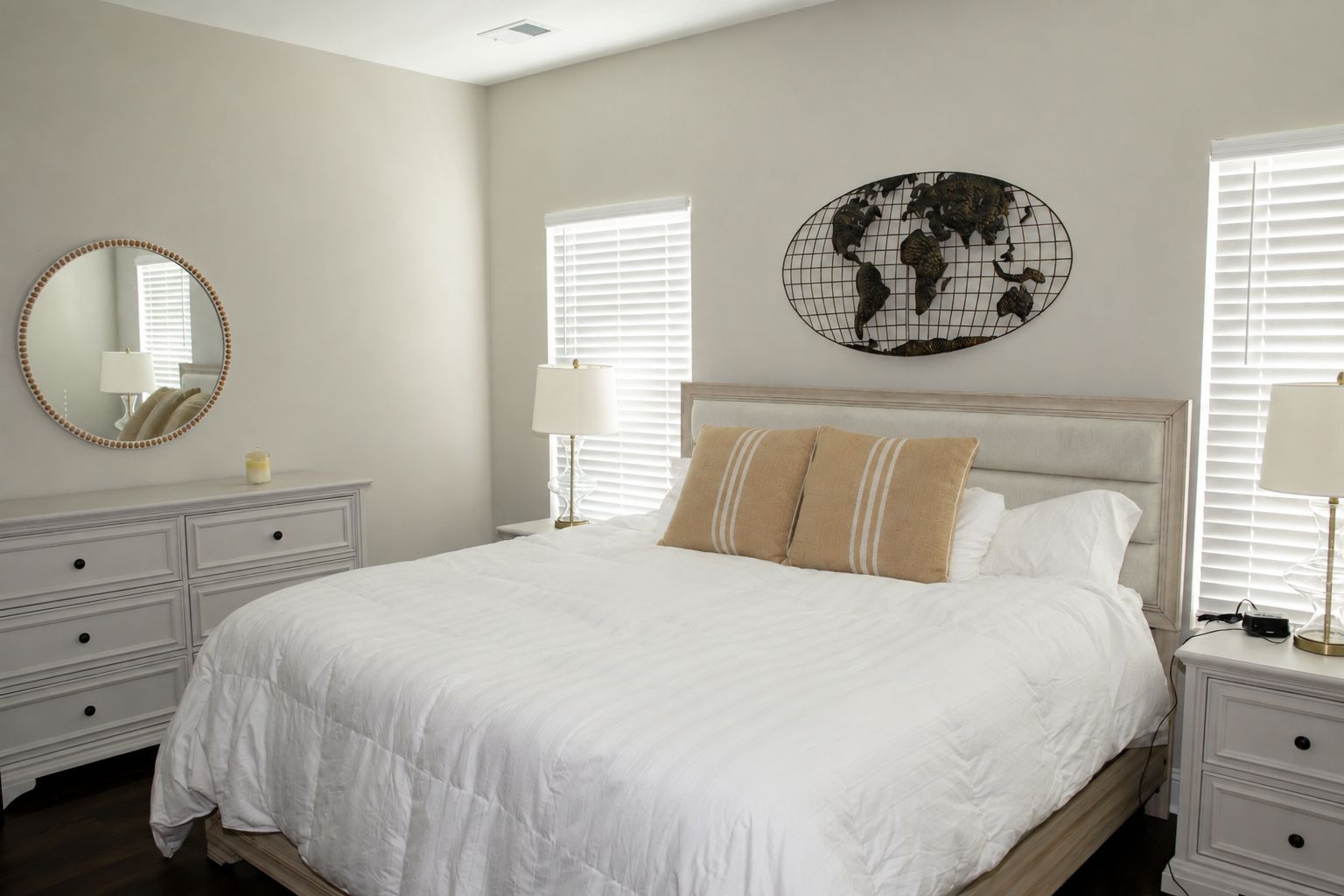 A bedroom with a large bed, two bedside tables, a round mirror, and a world map decoration.