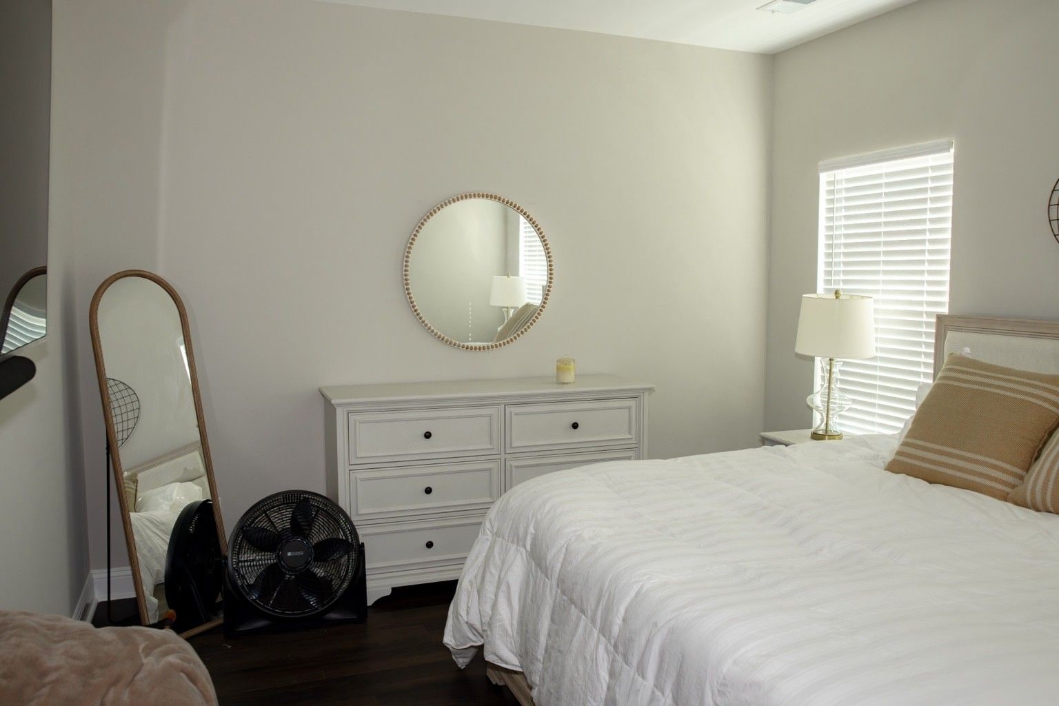 A bedroom with a bed, a dresser, a mirror, a fan, and a window with blinds.