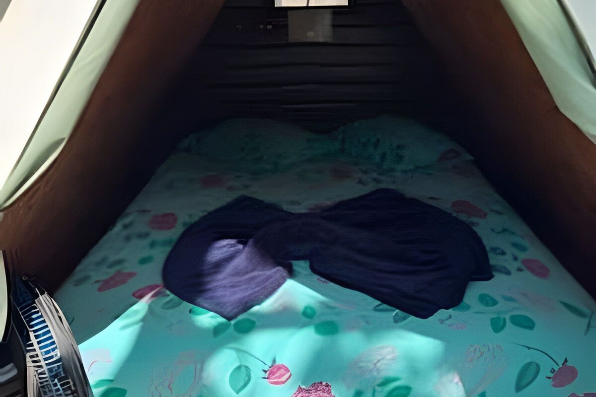 Una tienda de campaña con una cama en su interior, una pequeña mesa y un par de zapatos.
