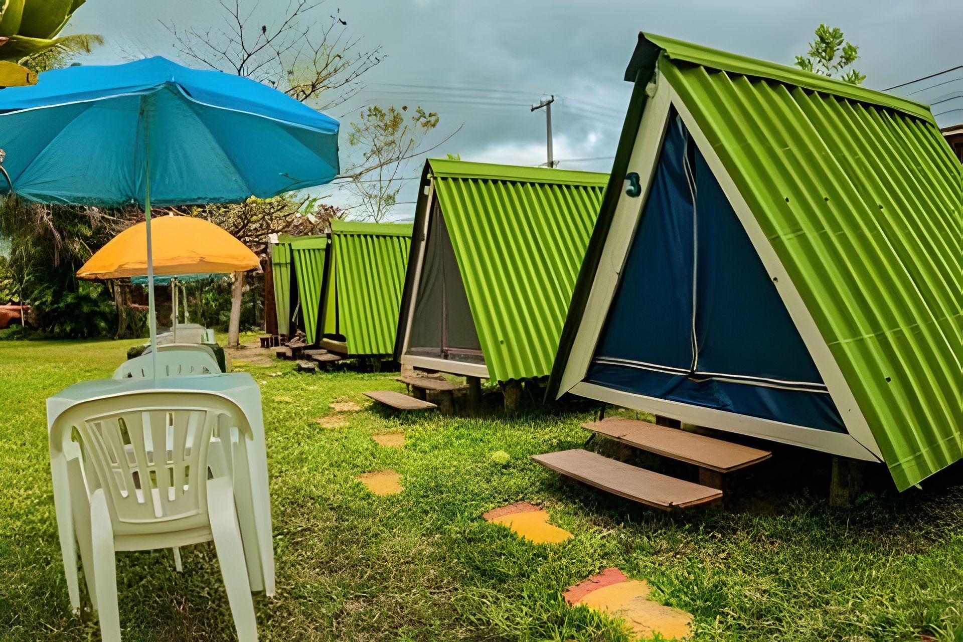 Outdoor camping-style accommodations with green roofs and blue walls, surrounded by grass and trees.
