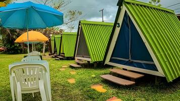 Outdoor camping-style accommodations with green roofs and blue walls, surrounded by grass and trees.