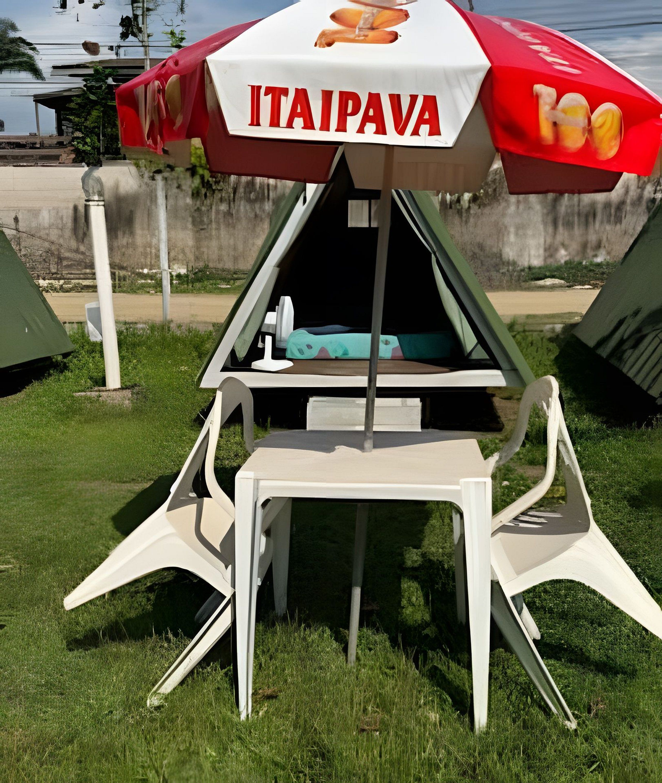 Una piccola zona salotto all'aperto con un ombrellone rosso e bianco con la scritta 'ITAIPAVA', un tavolo e due sedie.