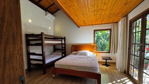 A room with a bunk bed, a single bed, a window with a view of greenery, and a wooden ceiling. - Vrbo Property (São Sebastião)
