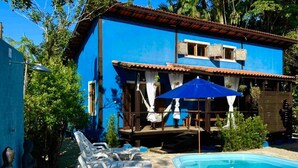 A blue building with a swimming pool, lounge chairs, and a covered seating area. - Vrbo Property (São Sebastião)