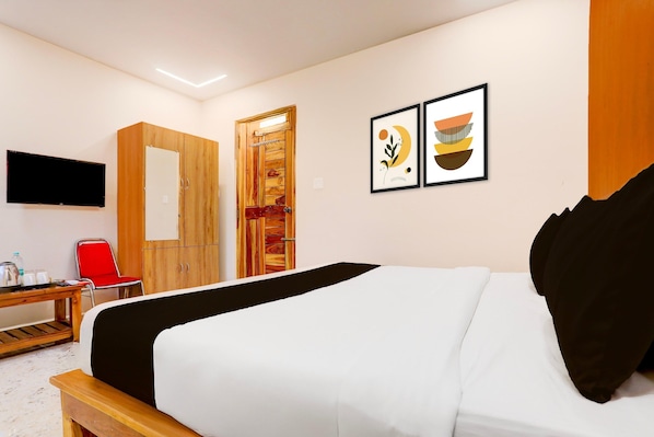 A hotel room with a bed, a desk with a chair, a television, and two framed artworks on the wall. - Premium Hotel Rama Grand (Tirupati)