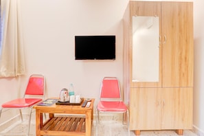 A room with a wooden cabinet, two red chairs, a small wooden table with a remote control, a water bottle, and a kettle. - Premium Hotel Rama Grand (Tirupati)