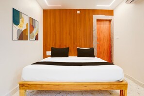 A hotel room with a bed, two black pillows, a wooden headboard, a wooden door, and abstract wall art.