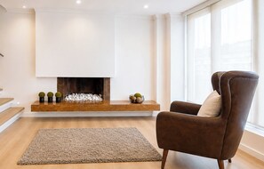 A modern living room with a fireplace, a brown leather armchair, and a patterned rug. - Apartamento Premium con terraza, a pasos de la Zona t/Parque 93/area 120 mts (Bogotá, D.C.)