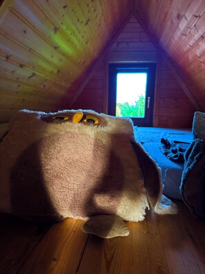 Ein gemütliches Dachzimmer mit Holzbalkendecke, einem Fenster mit Blick auf Grünflächen und einem flauschigen Gegenstand auf dem Boden.