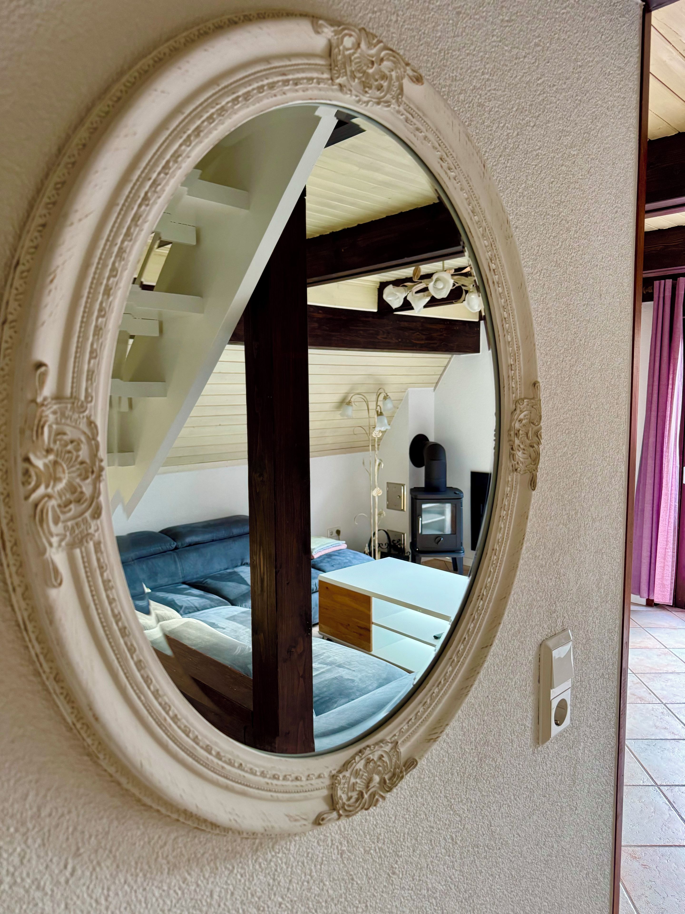Une pièce dotée d’un grand miroir décoratif qui reflète un escalier, un lit et une cheminée.