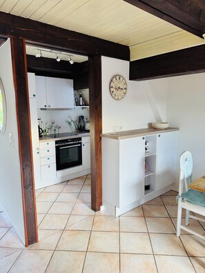 A compact kitchen with white cabinets, a clock on the wall, and a wooden-framed doorway. - A small house with a sauna, nestled in the apple orchard of the Altes Land region near Hamburg (Hollern-Twielenfleth)