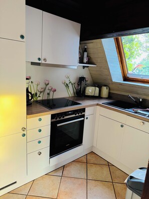 Une cuisine avec des meubles blancs, un four noir, une fenêtre et un plan de travail sur lequel se trouvent une bouilloire et un grille-pain.