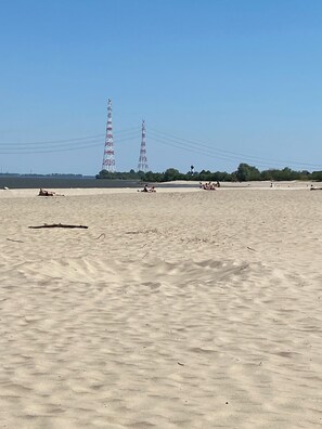Ein sandiger Strand mit Menschen und zwei hohen Sendetürmen in der Ferne.