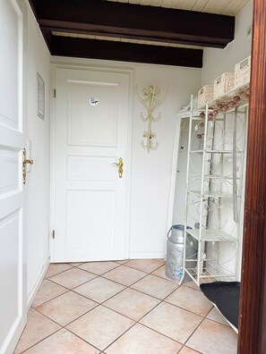 Une porte blanche avec une petite plaque, un porte-manteau en métal orné de boules décoratives et un sol carrelé.