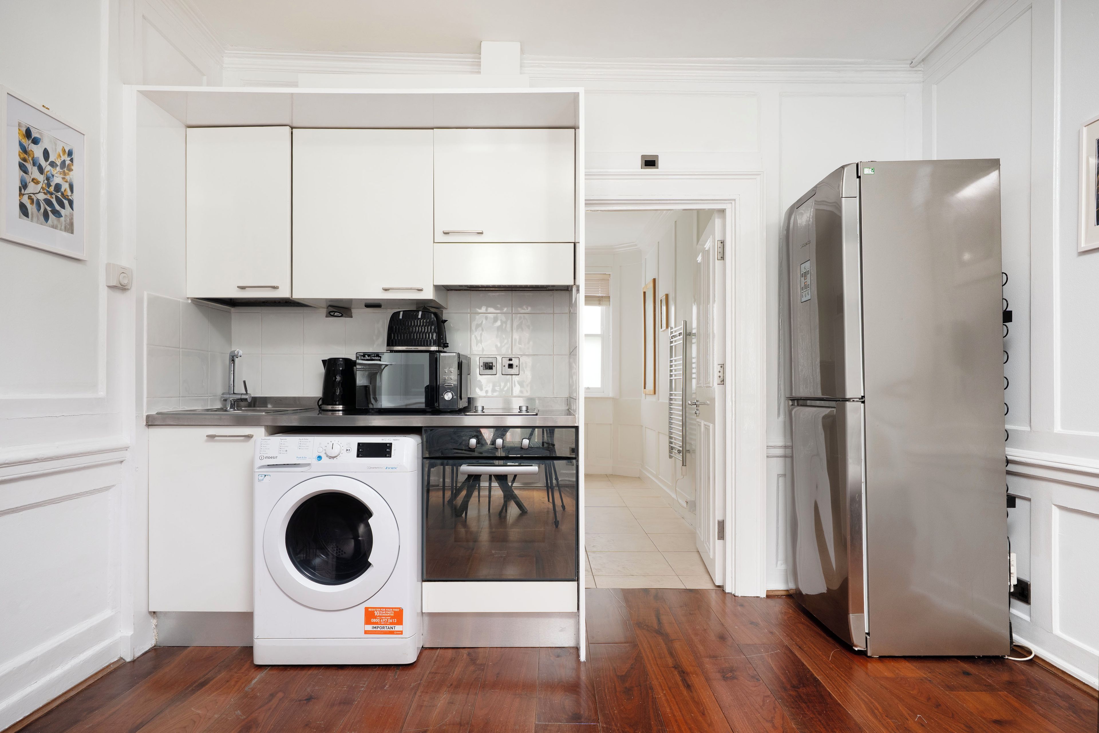 Una cocina moderna con armarios blancos, un refrigerador de acero inoxidable, una lavadora y una cafetera.