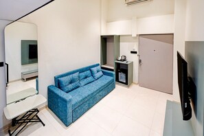 Un espacio habitable compacto con un sofá azul, una mesa pequeña, una kitchenette con cafetera y un televisor.