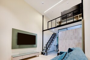 Una sala de estar moderna con un televisor de pantalla plana, un sofá y una escalera que lleva a un nivel superior.