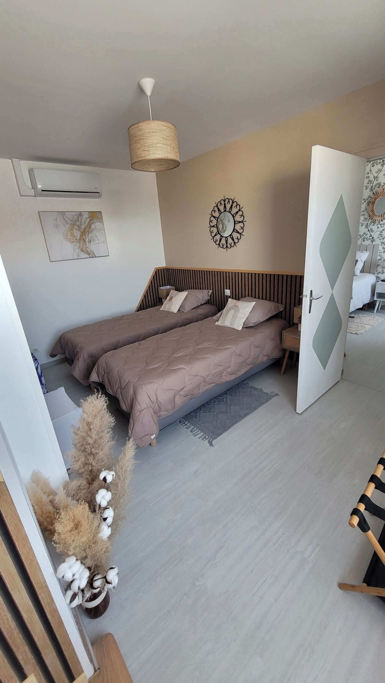 Un dormitorio moderno con dos camas, una lámpara colgante, un aire acondicionado de pared y un espejo decorativo.