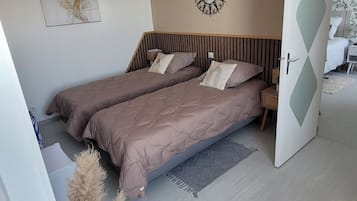 Un dormitorio moderno con dos camas, una lámpara colgante, un aire acondicionado de pared y un espejo decorativo.