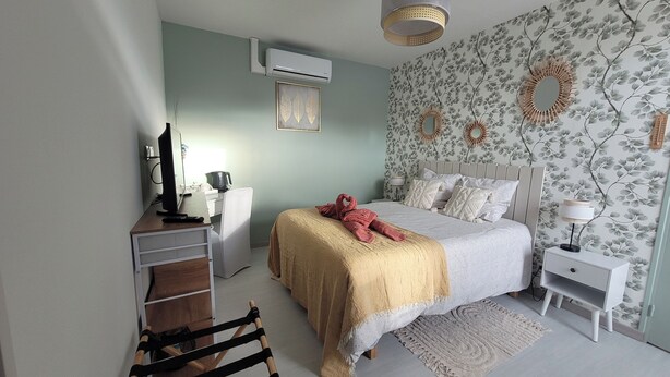 A bedroom with a bed, bedside tables, a desk, an air conditioner, and a chair. - The Travelers' Suite, a family suite that can accommodate up to 4 people and 1 infant (Saint-Christophe-de-Double)