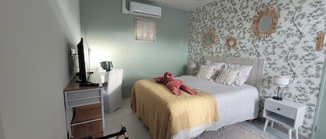 A bedroom with a bed, bedside tables, a desk, an air conditioner, and a chair.
