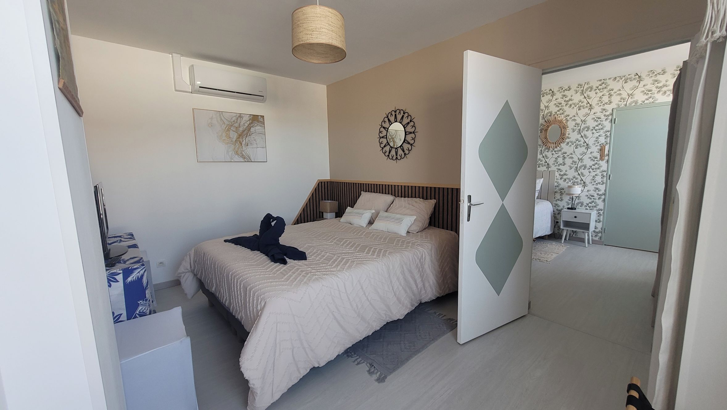 A bedroom with a bed, bedside table, lamp, wall clock, and an open door leading to another room.