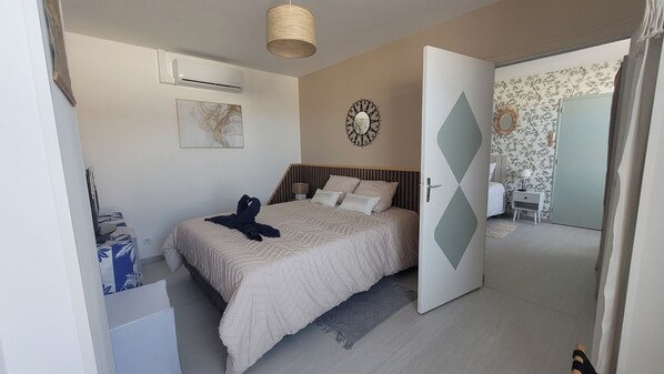 A bedroom with a bed, bedside table, lamp, wall clock, and an open door leading to another room.