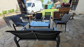 Een terras buiten met stenen vloer, een witte bestelwagen en een barbecue.